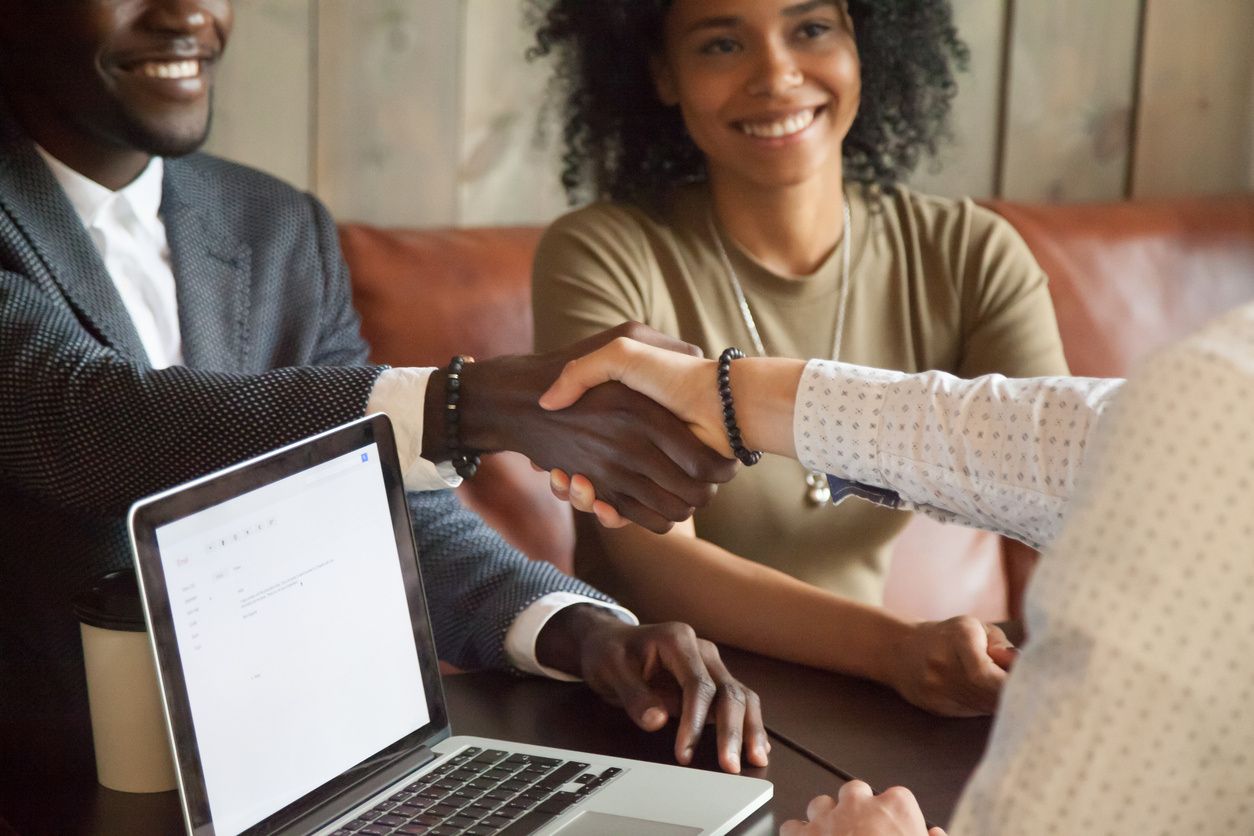 A woman shaking hands with another person in front of a laptop.