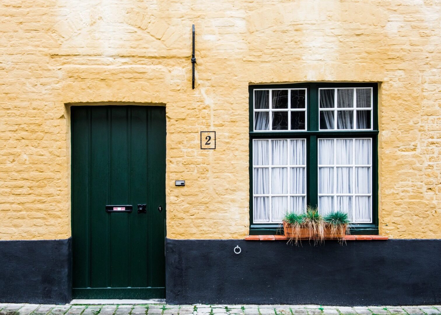 A green door and window on the side of a yellow brick building.