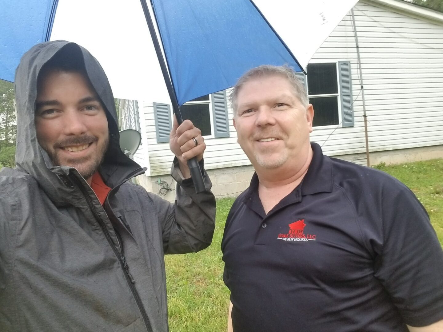 Two men holding an umbrella in front of a house.